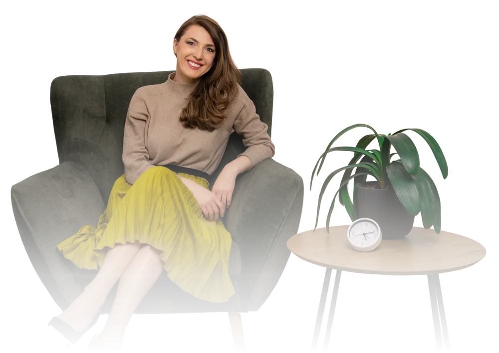 Andreea Giurgilă, life coach, zâmbind într-un fotoliu, lângă o măsuță cu plantă și ceas