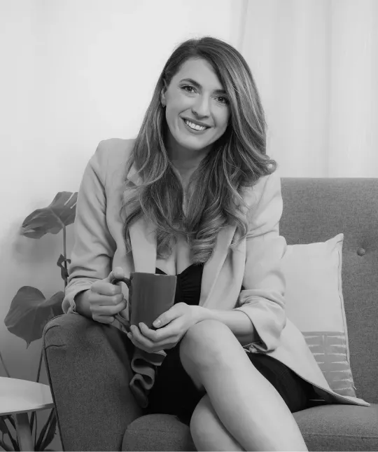 Andreea Giurgilă zâmbind, pe o canapea, cu o cană în mâini, fotografie alb-negru