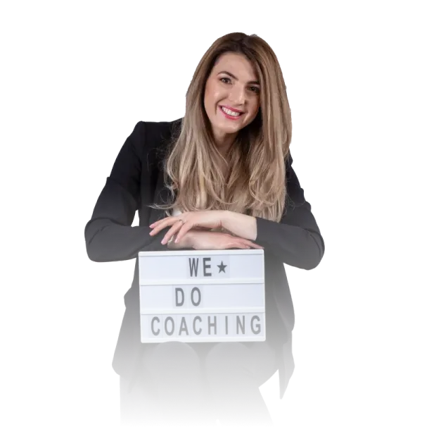 Andreea Giurgilă, life coach, zâmbind, cu o tăbliță luminoasă pe care scrie „We do coaching”