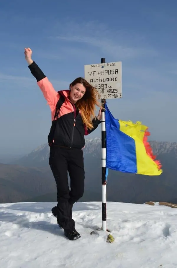 Andreea Giurgilă bucuroasă pe Vârful Păpușa, cu brațul ridicat, lângă indicator și tricolor