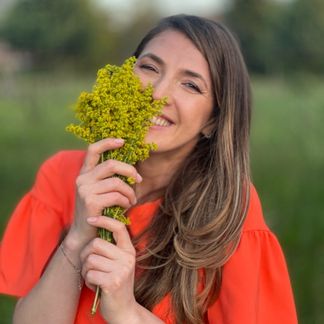 Andreea Giurgilă zâmbind, cu un buchet de flori galbene, coperta podcastului „Povestea mea ca om și coach”