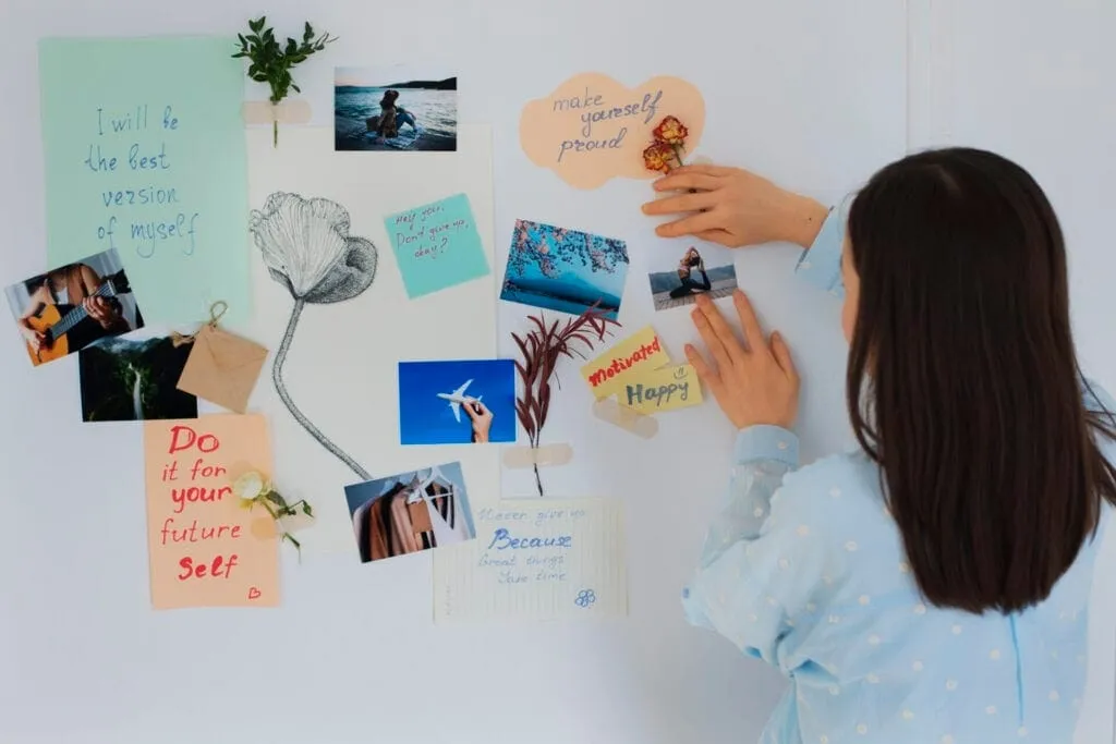Femeie care își compune pe perete un vision board din fotografii, flori uscate și mesaje
